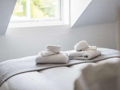 A bed with folded white towels near a window at Hoheck in Abersoch