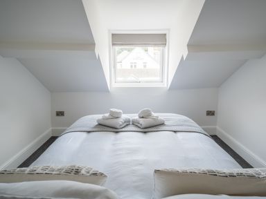 A bedroom with a bed facing a window under a slanted ceiling at Hoheck in Abersoch