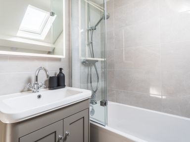 A bathroom with a sink cabinet a mirror a bathtub with shower and glass partition at Hoheck Abersoch
