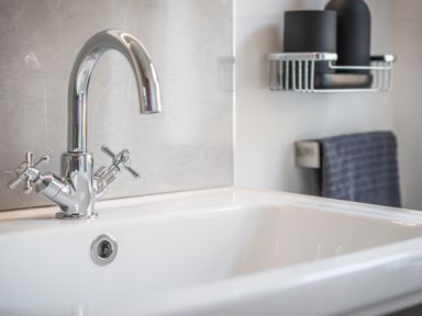 A close up of a bathroom sink with a chrome faucet and black containers on a wall shelf at Hoheck in Abersoch