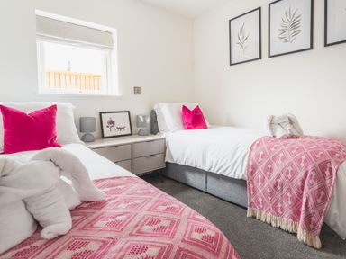 A bedroom with two single beds pink pillows and throws a nightstand with lamps and framed picture at Hoheck in Abersoch