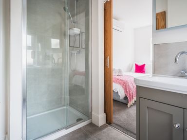 A bathroom with a glass shower enclosure and a sink looking into a bedroom with a bed and pink blanket at Hoheck in Abersoch