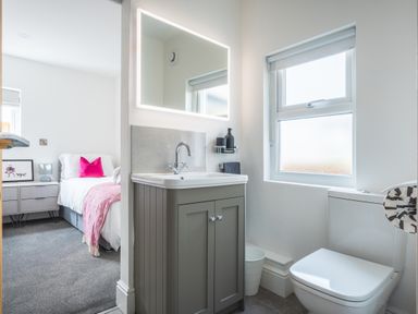 A bathroom with a sink vanity and mirror next to a window and toilet with a view of an adjacent bedroom at Hoheck in Abersoch