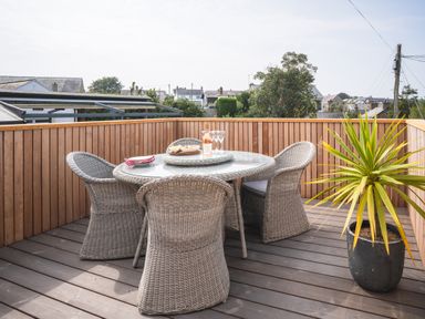 A balcony with a round glass table and four wicker chairs a potted plant on wooden deck at Hoheck in Abersoch