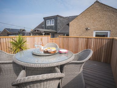 A patio with a round glass table and wicker chairs with snacks and wine at Hoheck in Abersoch