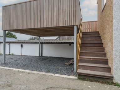 A wooden staircase leading up to a raised wooden deck with gravel ground underneath at Hoheck in Abersoch