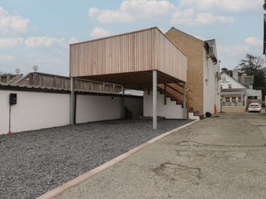An outdoor wooden structure on stilts with stairs leading up beside a building in a gravel and concrete area at Hoheck in Abersoch