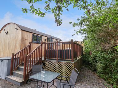 A small outdoor seating area with two chairs and a table next to wooden steps leading to a wooden cabin at The Retreat in Bangor-On-Dee