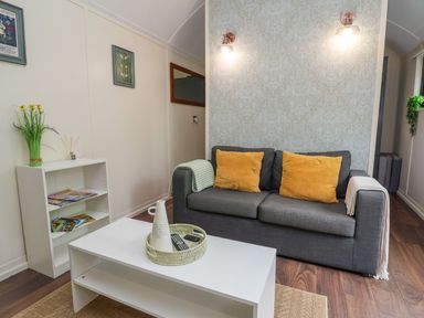 A living room with a gray sofa with yellow cushions a white coffee table and a small shelving unit at The Retreat in Bangor-On-Dee