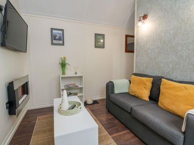 A living room with a gray sofa with yellow pillows a white coffee table a wall-mounted television and a fireplace at The Retreat in Bangor-On-Dee