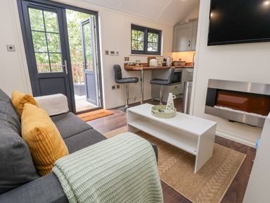 A living room with a gray sofa yellow pillows a white coffee table a wall-mounted television and an electric fireplace at The Retreat in Bangor-On-Dee