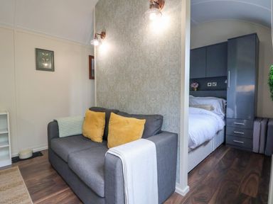 A gray sofa with yellow pillows next to a bed and dark gray cabinets at The Retreat in Bangor-On-Dee
