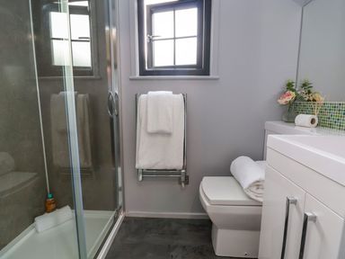 A bathroom with a shower enclosure a toilet a towel rack with towels and a vanity unit at The Retreat in Bangor-On-Dee