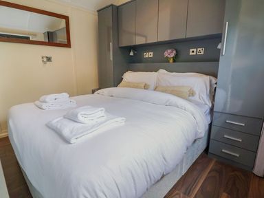 A bedroom with a double bed white linens towels on the bed grey cabinets and a wall mirror at The Retreat in Bangor-On-Dee