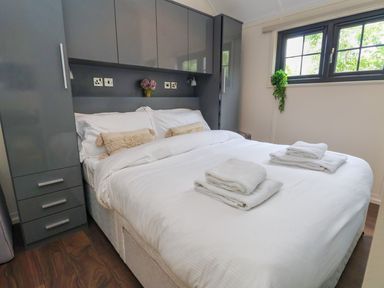 A bedroom with a double bed white linens grey built in cupboards and a window with greenery outside at The Retreat in Bangor-On-Dee