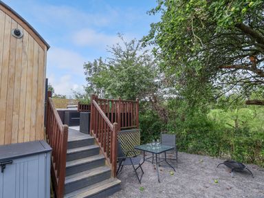 An outdoor area with stairs leading to a wooden deck with seating and a glass table with two chairs under a tree at The Retreat in Bangor-On-Dee