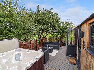 An outdoor deck with a hot tub seating area wooden railing and an open door at The Retreat in Bangor-On-Dee
