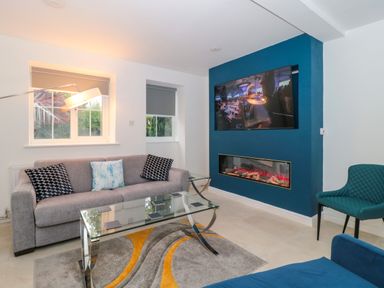 A living room with a grey sofa and cushions glass coffee table wall mounted tv and electric fireplace at 4 Noel Court in Chipping Campden