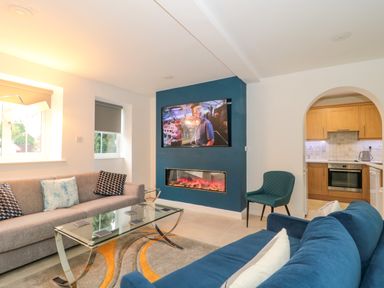 A living room with sofas a glass coffee table a mounted television and an electric fireplace at 4 Noel Court in Chipping Campden