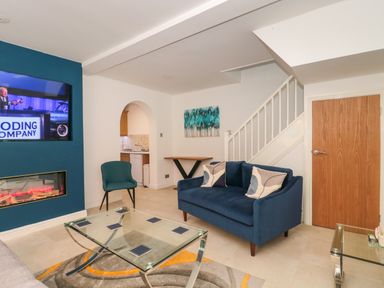A living room with a blue sofa and chair glass coffee table and mounted TV above fireplace at 4 Noel Court in Chipping Campden