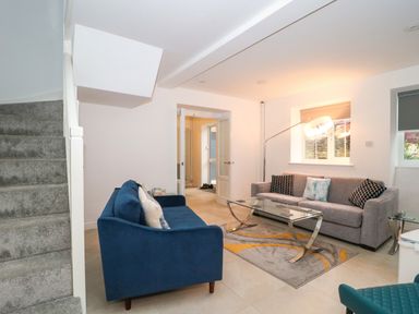 A living room with two sofas a glass coffee table a floor lamp and a staircase at 4 Noel Court in Chipping Campden