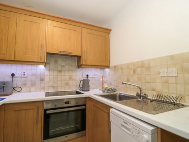 A kitchen with wooden cabinets, an electric stove, an oven, a sink, a dishwasher, and a tiled backsplash at 4 Noel Court in Chipping Campden