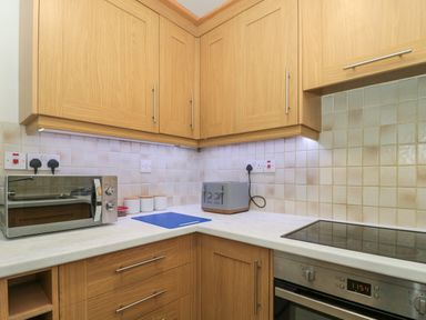 A kitchen corner with wooden cabinets a microwave a toaster a cutting board electric stove and oven at 4 Noel Court in Chipping Campden