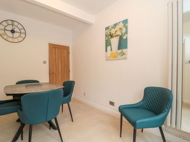 A dining area with a table and blue chairs a wooden door and a wall clock at 4 Noel Court in Chipping Campden