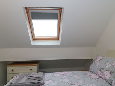 A bedroom with a floral bedspread gray towels on the bed a chest of drawers and a skylight window at 4 Noel Court in Chipping Campden
