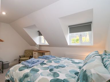 A bedroom with a bed with patterned bedding and folded towels next to two windows with blinds at 4 Noel Court in Chipping Campden