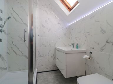 A bathroom with a shower, wall-mounted sink, toilet, skylight window, and tiled walls at 4 Noel Court in Chipping Campden