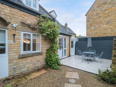 An outdoor patio with stone walls a gravel path a metal table with chairs and an umbrella at 4 Noel Court in Chipping Campden