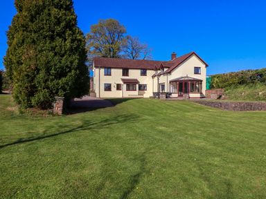 A two-story house with beige walls and brown roof with a large green lawn in front at Valley House in Halberton near Tiverton