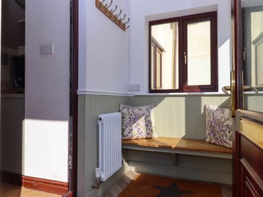 A small entryway with a wooden bench with floral cushions a radiator and a window at Valley House in Halberton near Tiverton