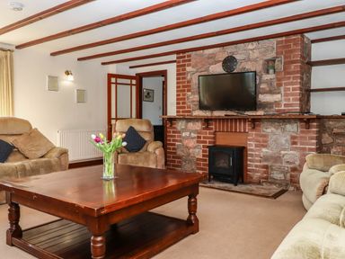 A living room with beige armchairs a wooden coffee table with flowers a mounted television and a brick fireplace at Valley House Halberton near Tiverton