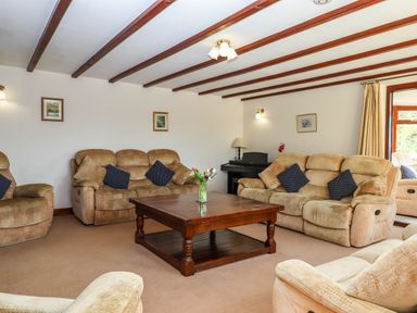 A living room with beige sofas a wooden coffee table and ceiling beams at Valley House Halberton near Tiverton
