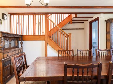 A dining room with wooden table and chairs near wooden staircase and cabinets at Valley House Halberton near Tiverton