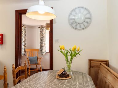 A dining area with a table covered by a patterned tablecloth with yellow tulips in a vase and a plate of brownies under a glass cover at Valley House in Halberton near Tiverton