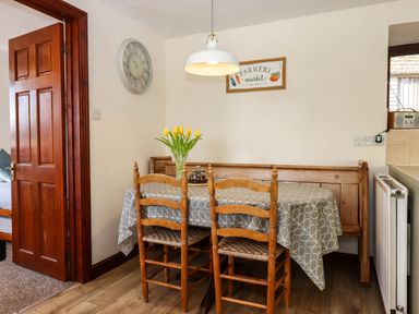 A dining area with wooden chairs a table with a patterned tablecloth a bench and a vase of yellow tulips at Valley House in Halberton near Tiverton