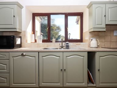 A kitchen countertop with a sink microwave kettle and compost bin under a window at Valley House in Halberton near Tiverton