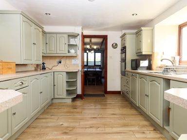 A kitchen with light green cabinets a wooden breadbox microwave and a sink with a window at Valley House in Halberton near Tiverton