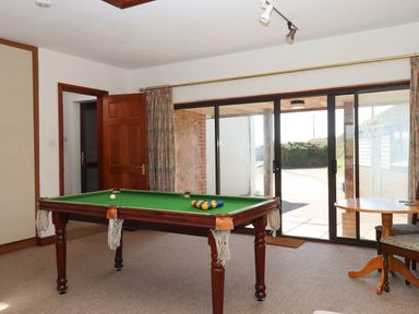 A room with a pool table near a wooden door and sliding glass doors with a round table and chairs near the windows at Valley House in Halberton near Tiverton