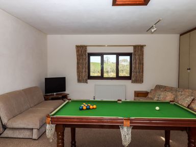 A game room with a pool table two sofas a small television and a window showing outdoor scenery at Valley House in Halberton near Tiverton