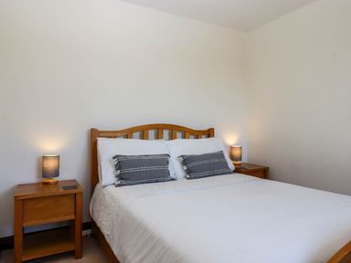 A bedroom with a wooden bed, two gray pillows, white bedding, wooden bedside tables, and lamps at Valley House in Halberton near Tiverton