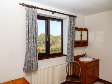 A wooden chair and sink cabinet next to a window with curtains at Valley House Halberton near Tiverton