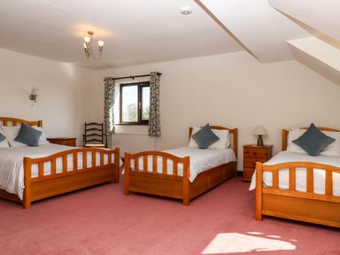 A bedroom with three wooden beds a window with curtains a chair and bedside tables at Valley House Halberton near Tiverton
