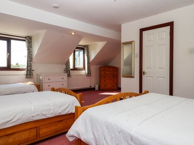 A bedroom with two wooden beds white bedding pink carpet and two dressers at Valley House Halberton near Tiverton
