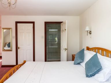 A bedroom with a wooden bed with white bedding and blue pillows next to two white doors one open to a tiled shower at Valley House in Halberton near Tiverton