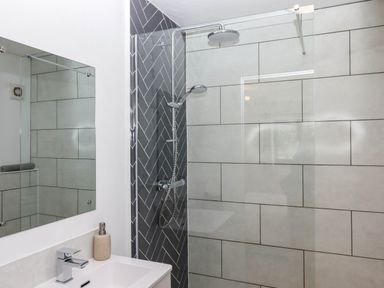A bathroom with a sink faucet mirror and shower area with glass partition and tiled walls at Valley House in Halberton near Tiverton