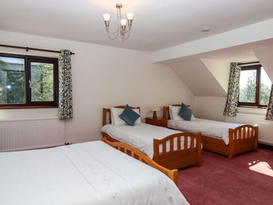 A bedroom with three single beds bedside table lamp and two windows with curtains at Valley House in Halberton near Tiverton